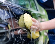 Female hand with yellow sponge washing car